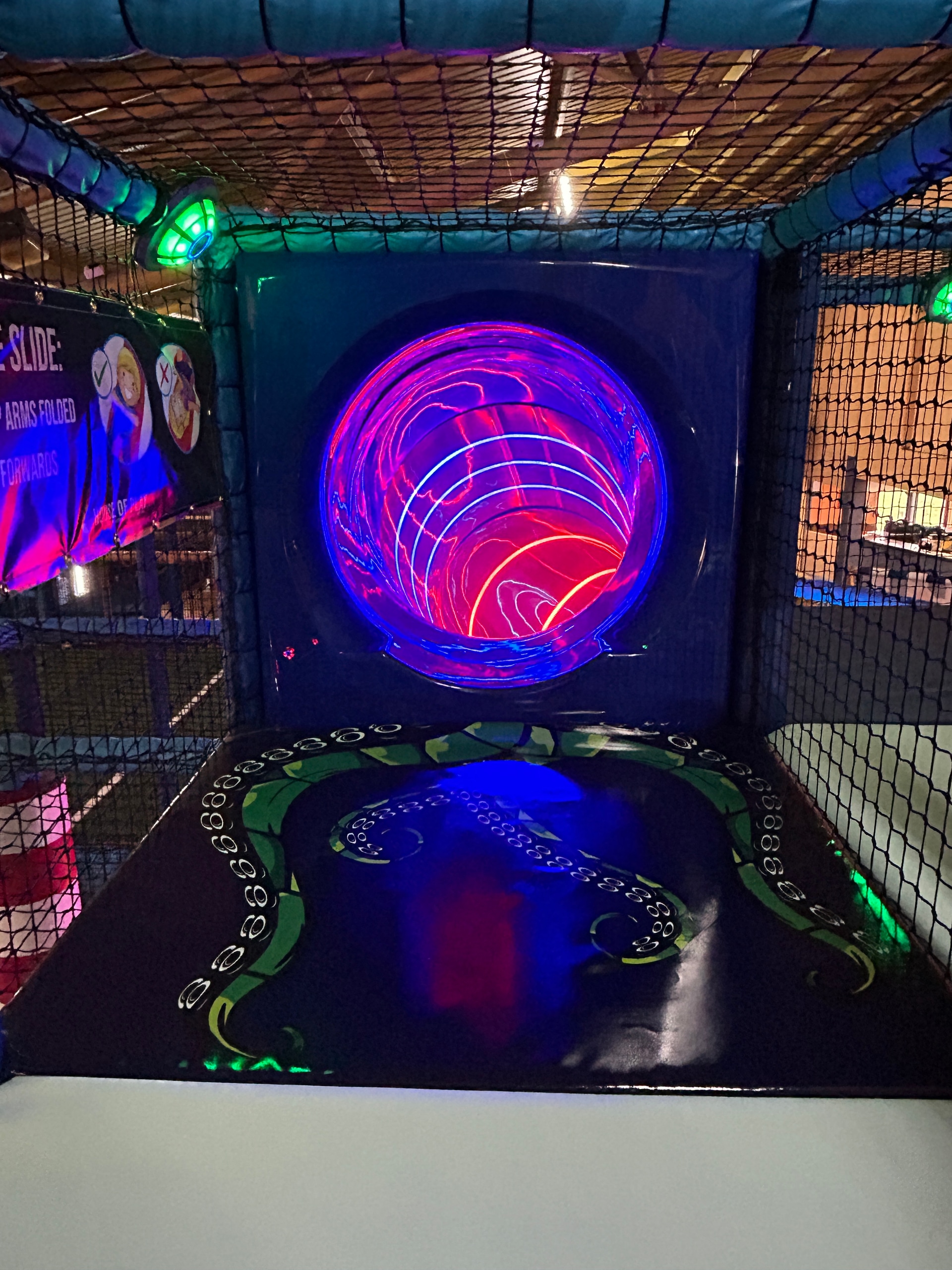 Soft play entrance into the LED spiral slide with octopus floor graphic and glowing tunnel
