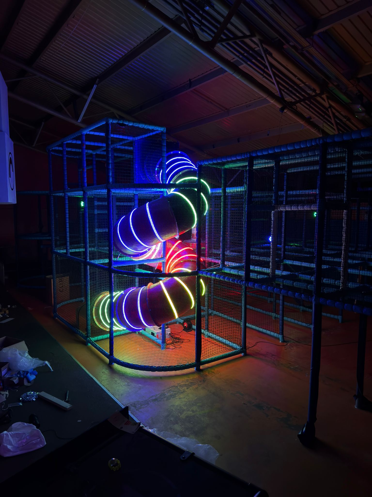 Dark indoor play frame with a multi-colour LED spiral slide glowing inside the netting