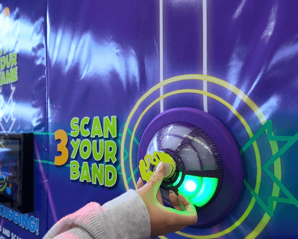 A player tapping a Ninja Tag wristband on a glowing pod beside Scan Your Band graphics