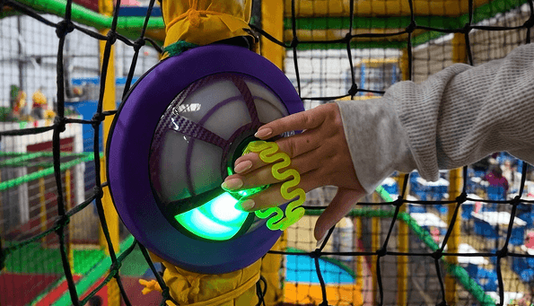 A Ninja Tag wristband touching a glowing pod mounted on yellow-padded play equipment